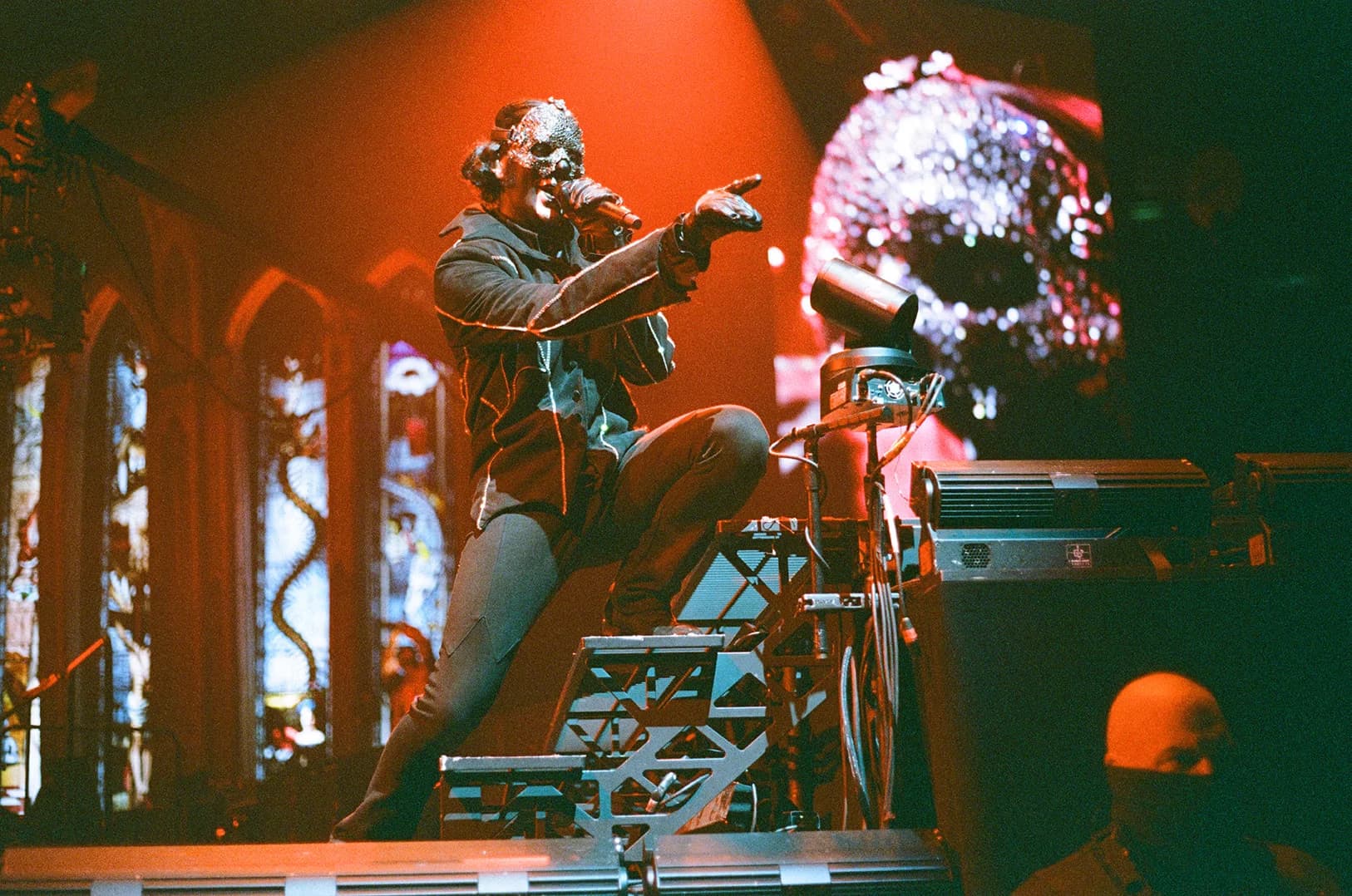 A performer in dark clothing points into the crowd on a dimly lit stage.