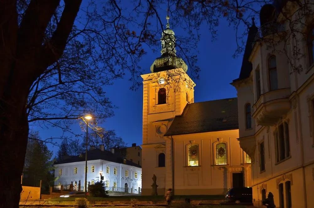 Historyczny kamienny kościół jest oświetlony w nocy na tle ciemnoniebieskiego wieczornego nieba.