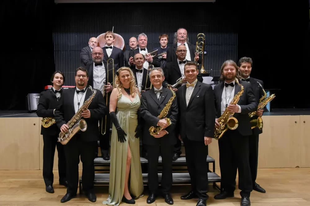 Jazzový big band pózuje na pódiu ve společenském večerním oblečení pro společnou fotografii.