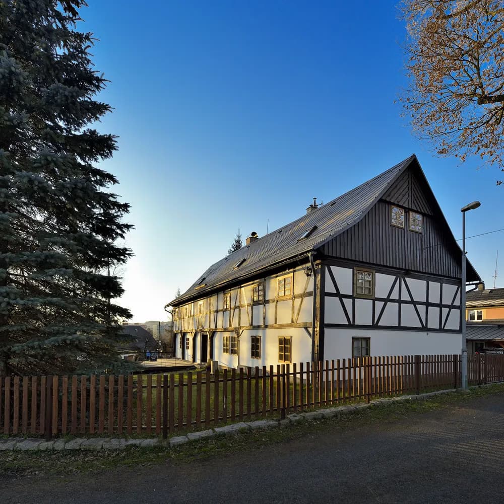 Ein traditionelles Fachwerkhaus steht hinter einem Holzzaun unter einem klaren blauen Himmel.