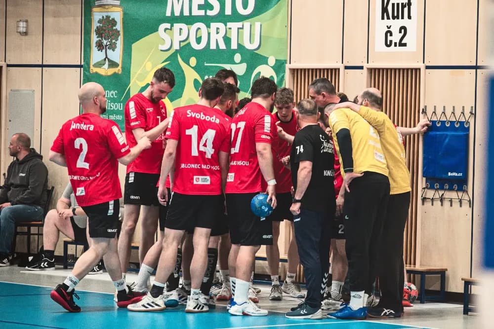 Drużyna piłkarzy ręcznych w koszulkach zbiera się w krąg na hali sportowej.