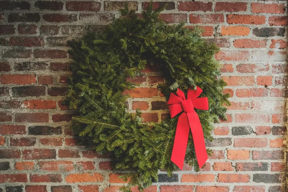 Ein üppiger Weihnachtskranz mit großer roter Schleife hängt an einer rustikalen Ziegelwand.