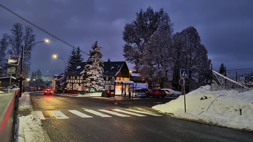Verschneite Straßenszene mit einem Fachwerkhaus in der Dämmerung, inklusive Zebrastreifen und Bäumen.