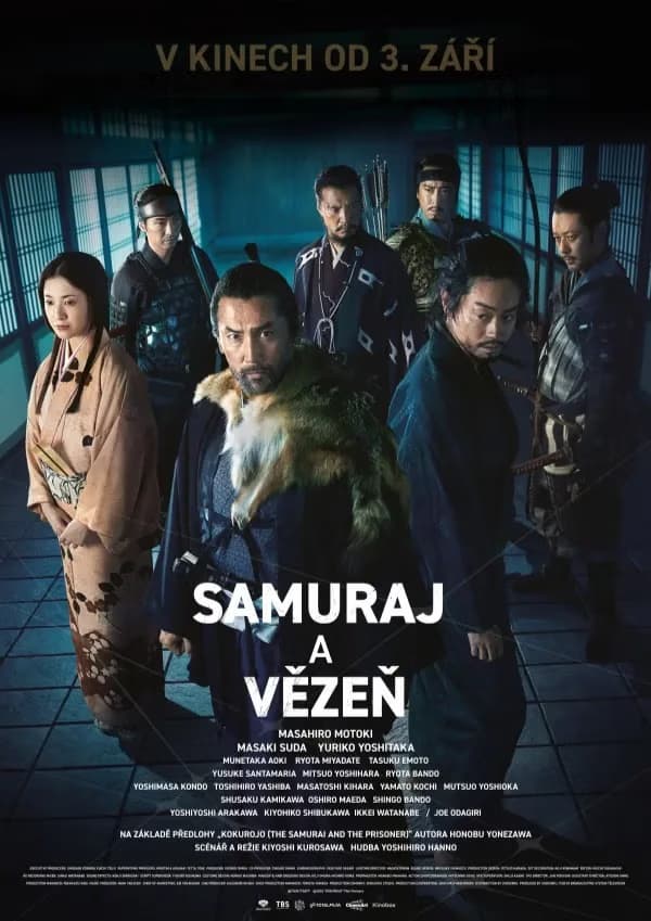 A cast of Japanese actors in traditional period clothing stands in a dimly lit hallway.