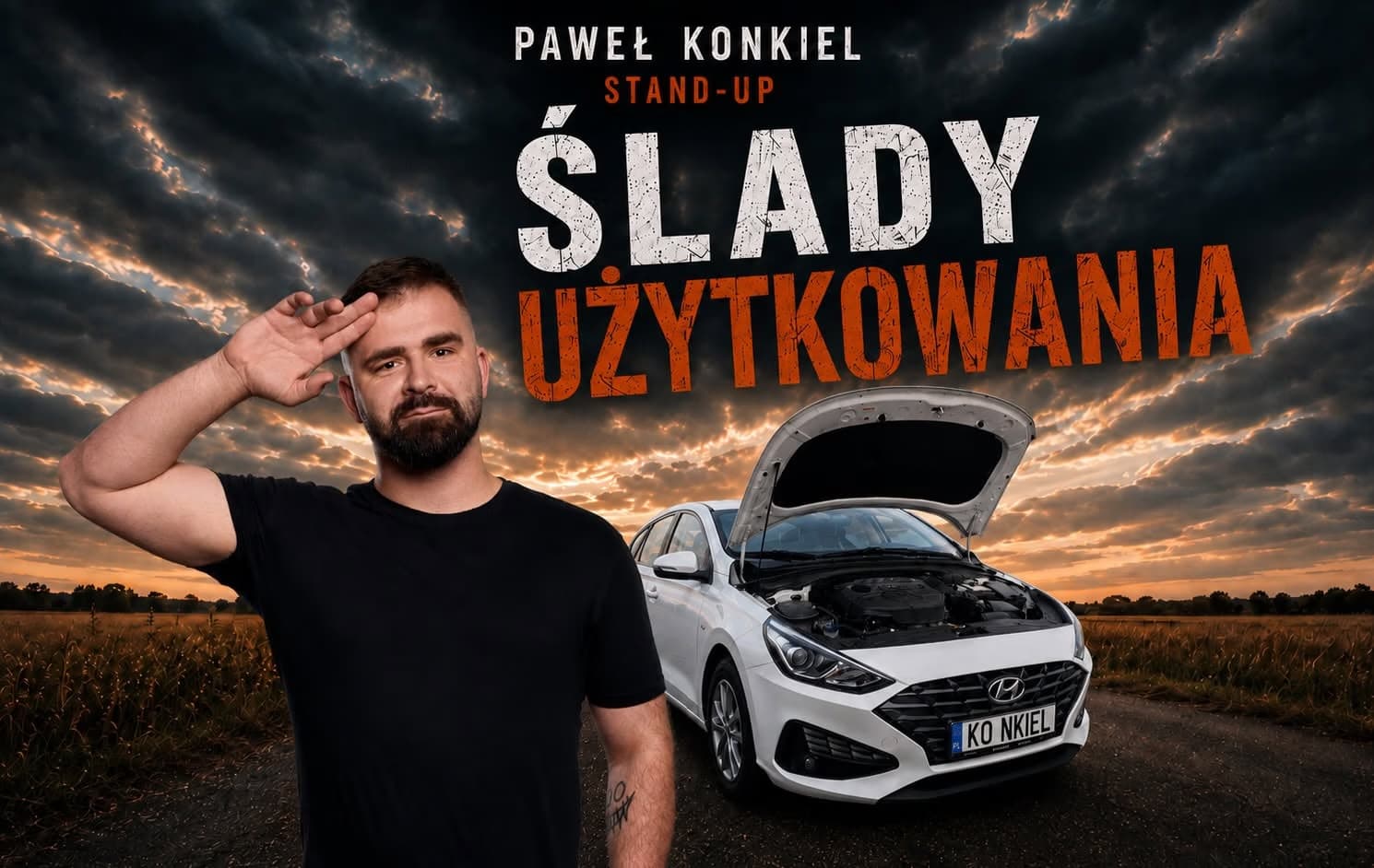 A man in a black shirt stands beside a white car with its hood open in a field at sunset.