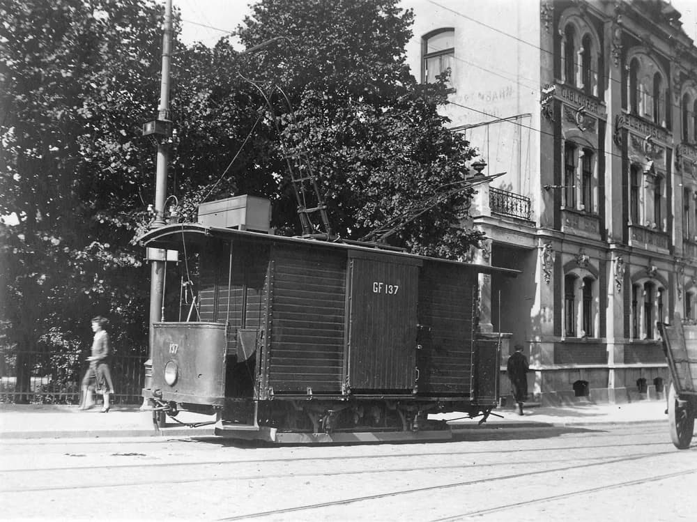 Černobílý historický snímek nákladní tramvaje v ulicích města.