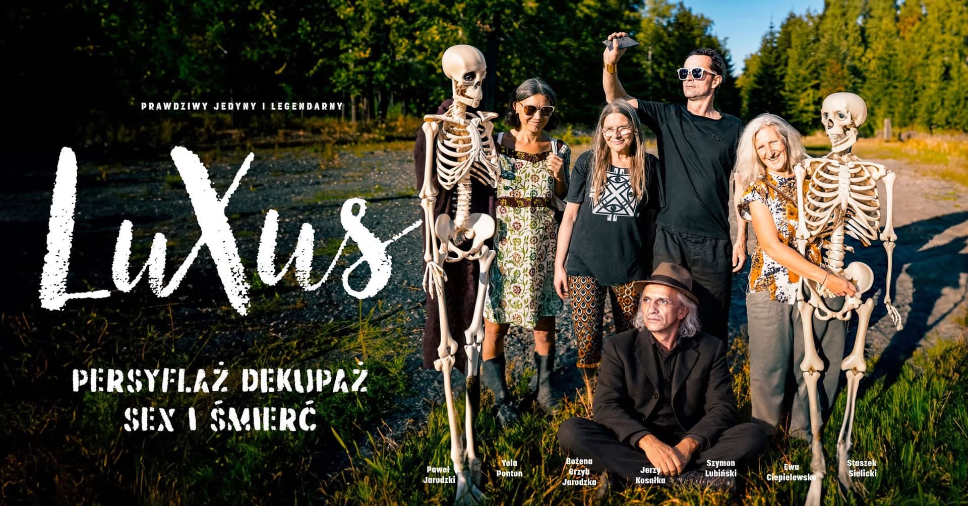 Grupa ludzi pozuje na zewnątrz do zdjęcia w towarzystwie dwóch ludzkich szkieletów.