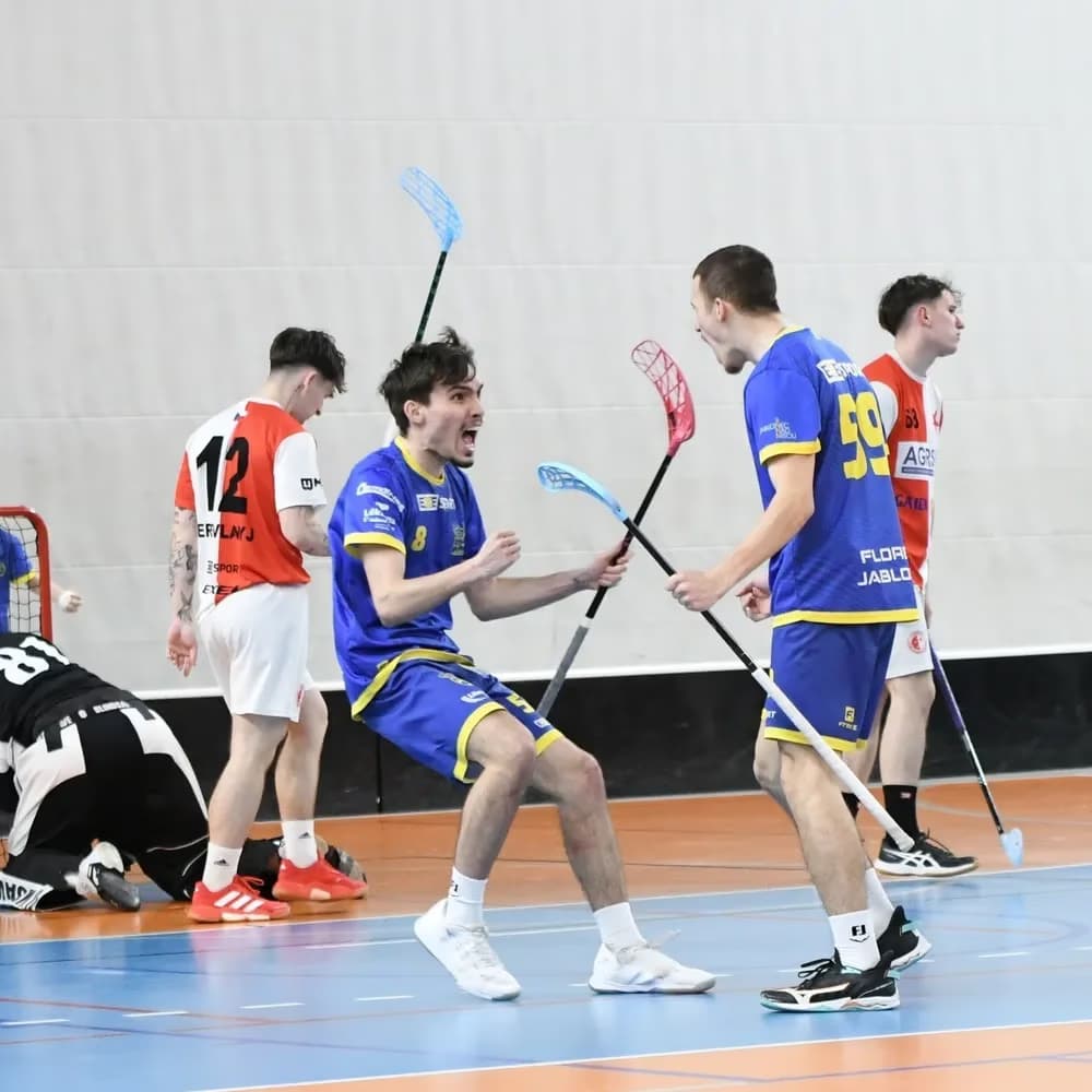Floorball players in blue uniforms celebrate a goal on the court during a competitive match.