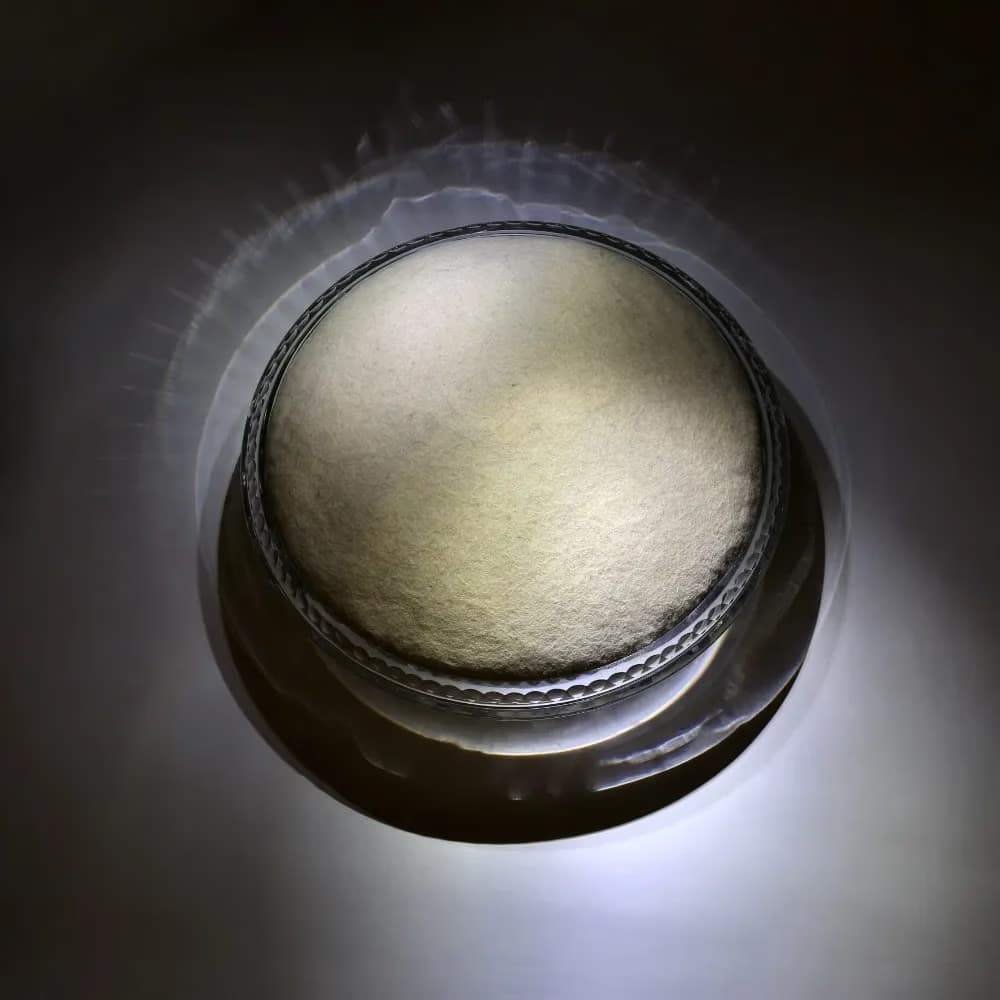 A circular metallic container with a textured lid is brightly illuminated against a dark background.