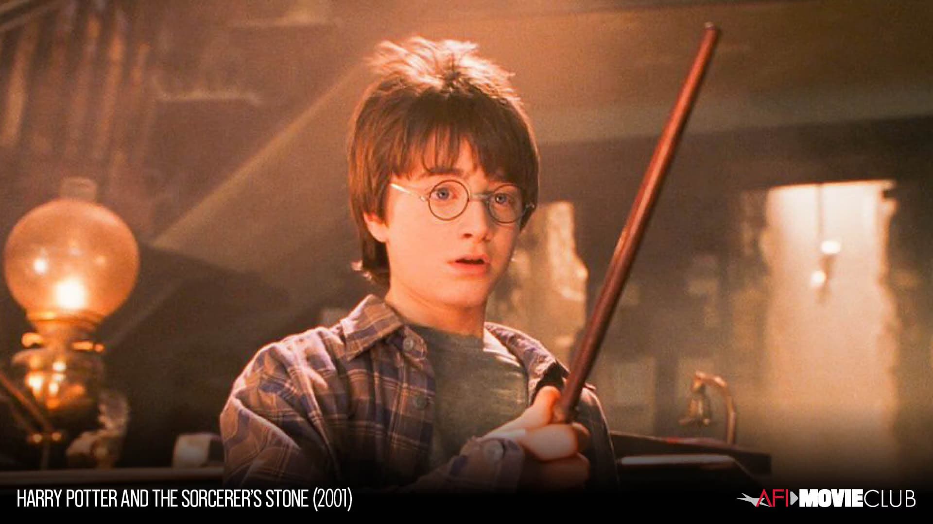 Young Harry Potter wearing glasses holds a wand inside a dimly lit room with a warm lamp.