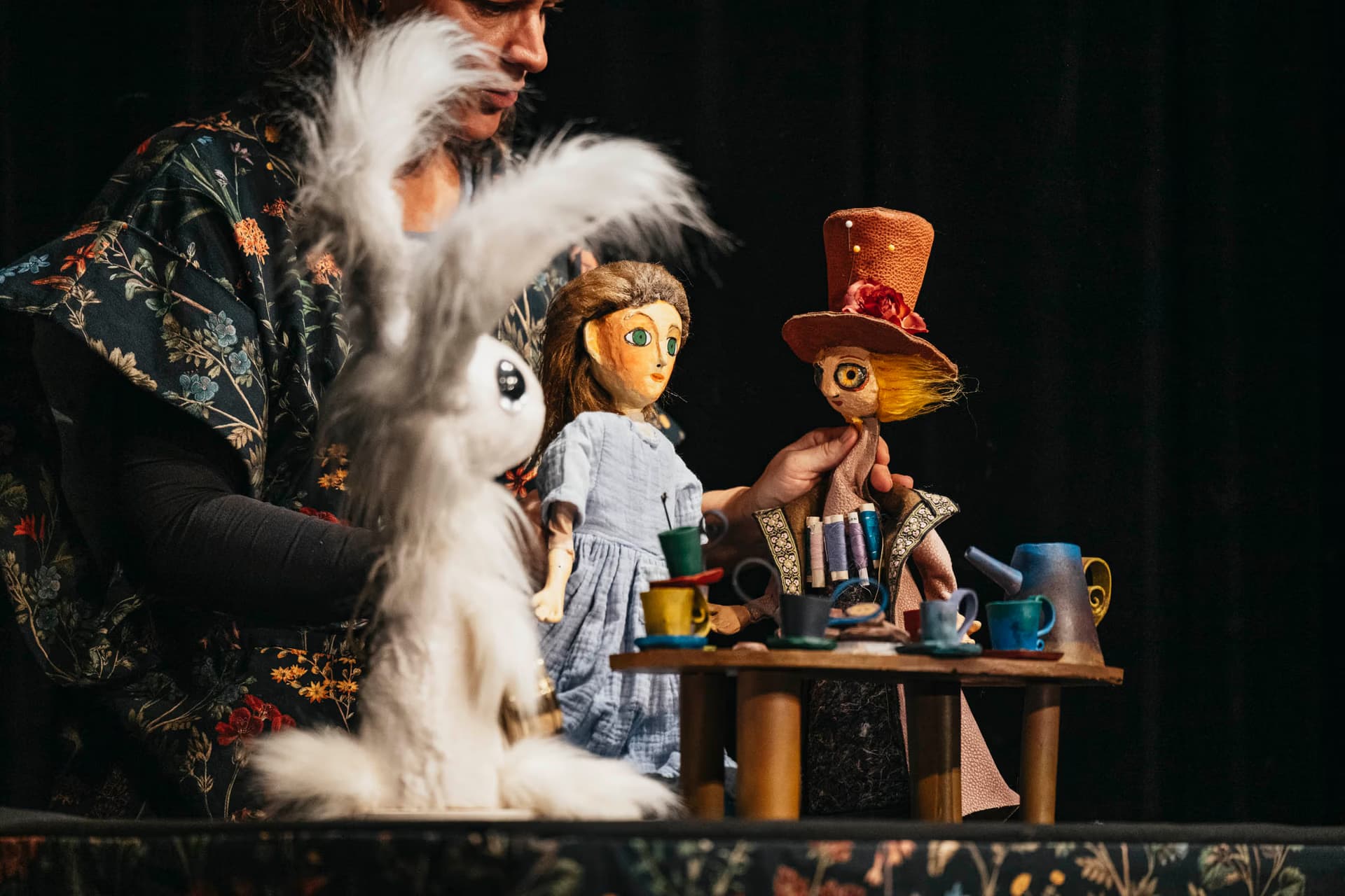 Ein Puppenspieler führt eine Szene mit Figuren von Alice, dem Hutmacher und dem weißen Kaninchen auf.