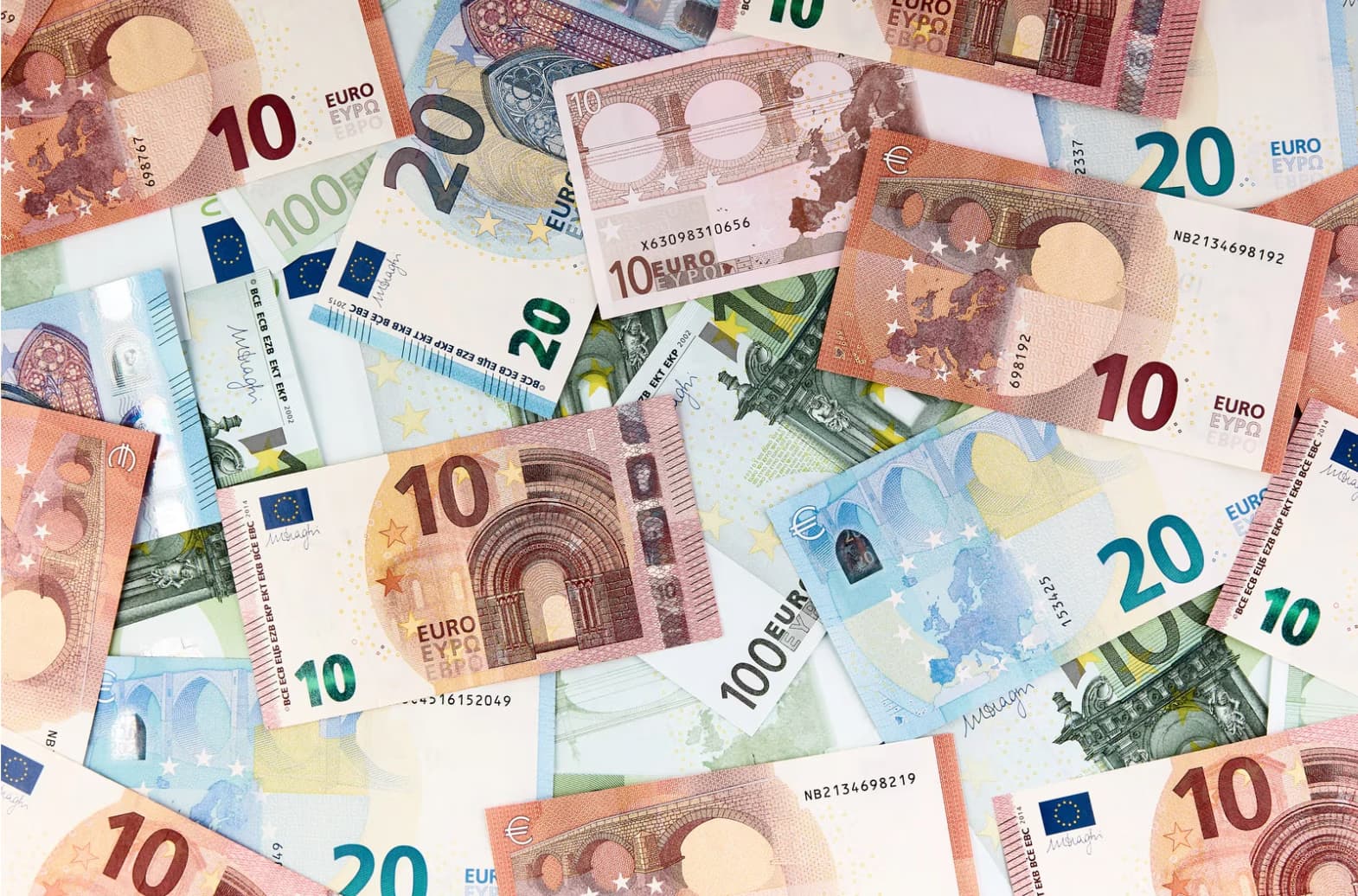 A scattered pile of various ten and twenty Euro banknotes overlaps on a flat surface.
