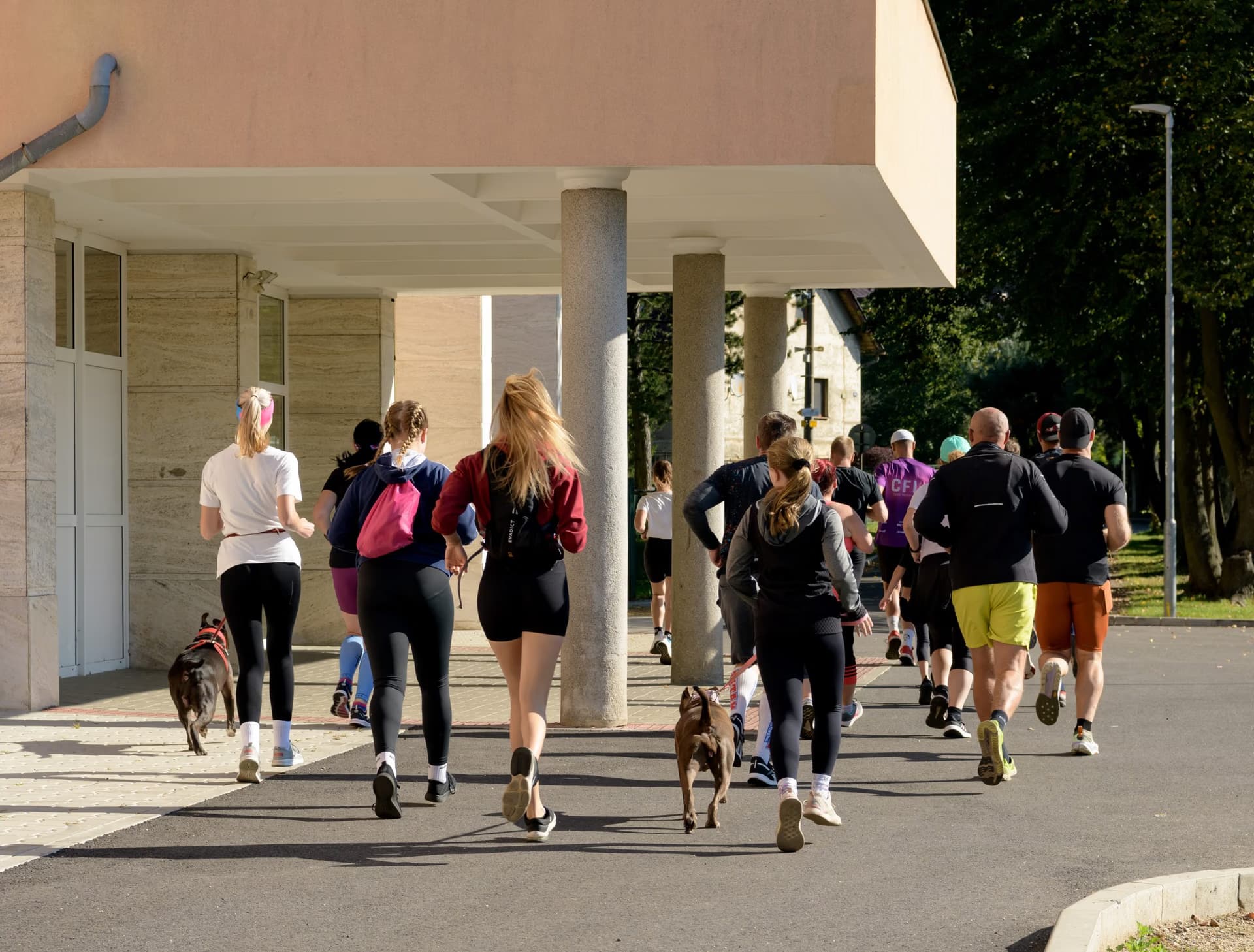 Eine Gruppe von Läufern joggt an einem sonnigen Tag auf einem gepflasterten Weg an einem modernen Gebäude entlang.