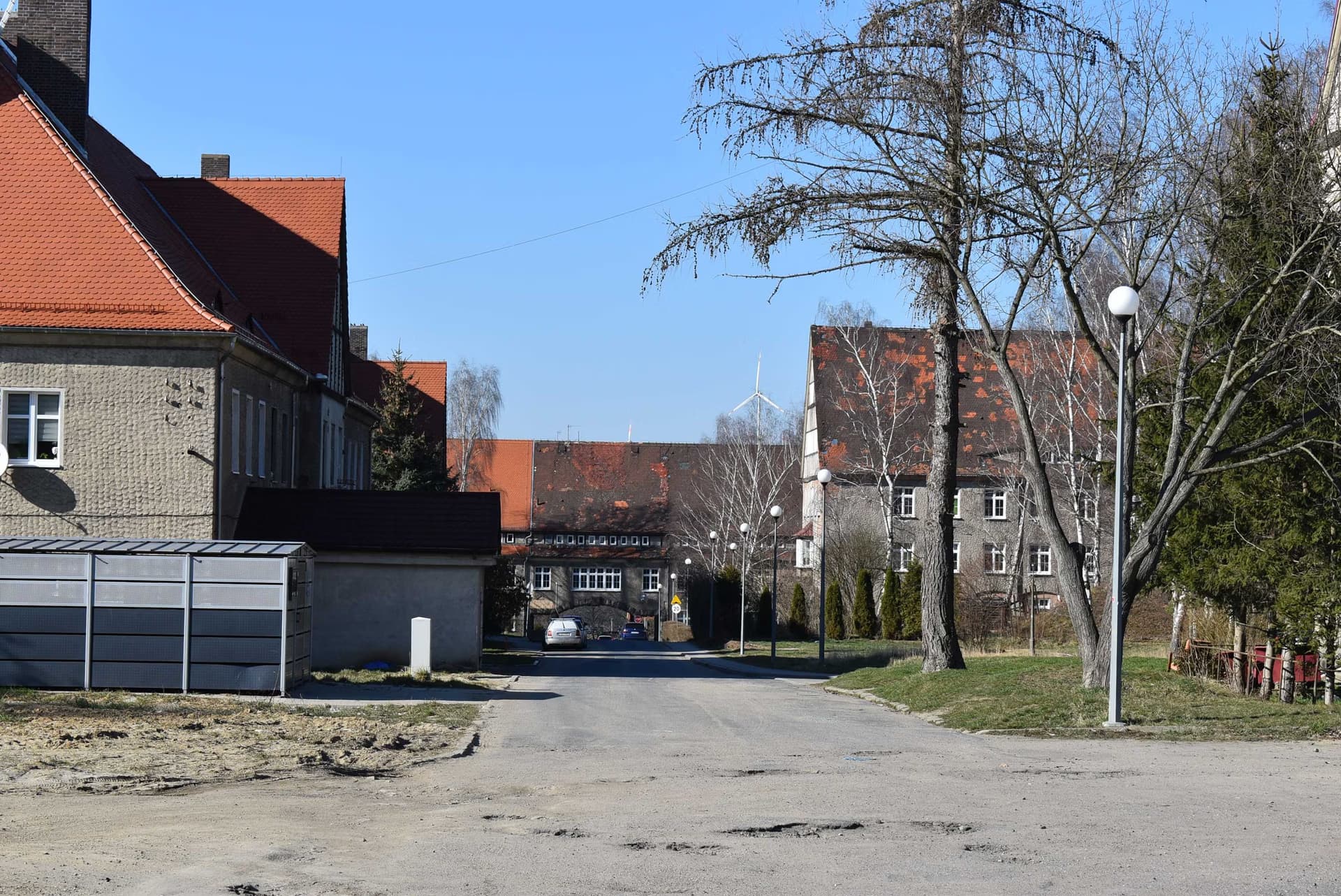 A quiet paved street passes between old brick buildings with orange tiled roofs.