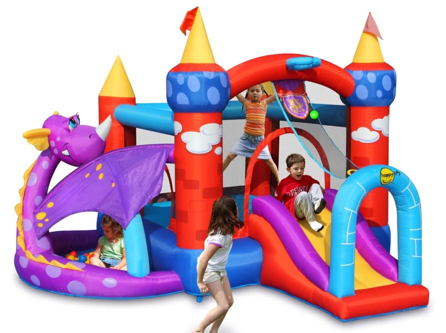 Three children play on a colorful inflatable castle with a dragon design and a small slide.