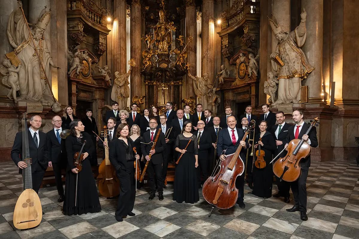 Classical orchestra with instruments poses inside a grand, ornately decorated church interior.