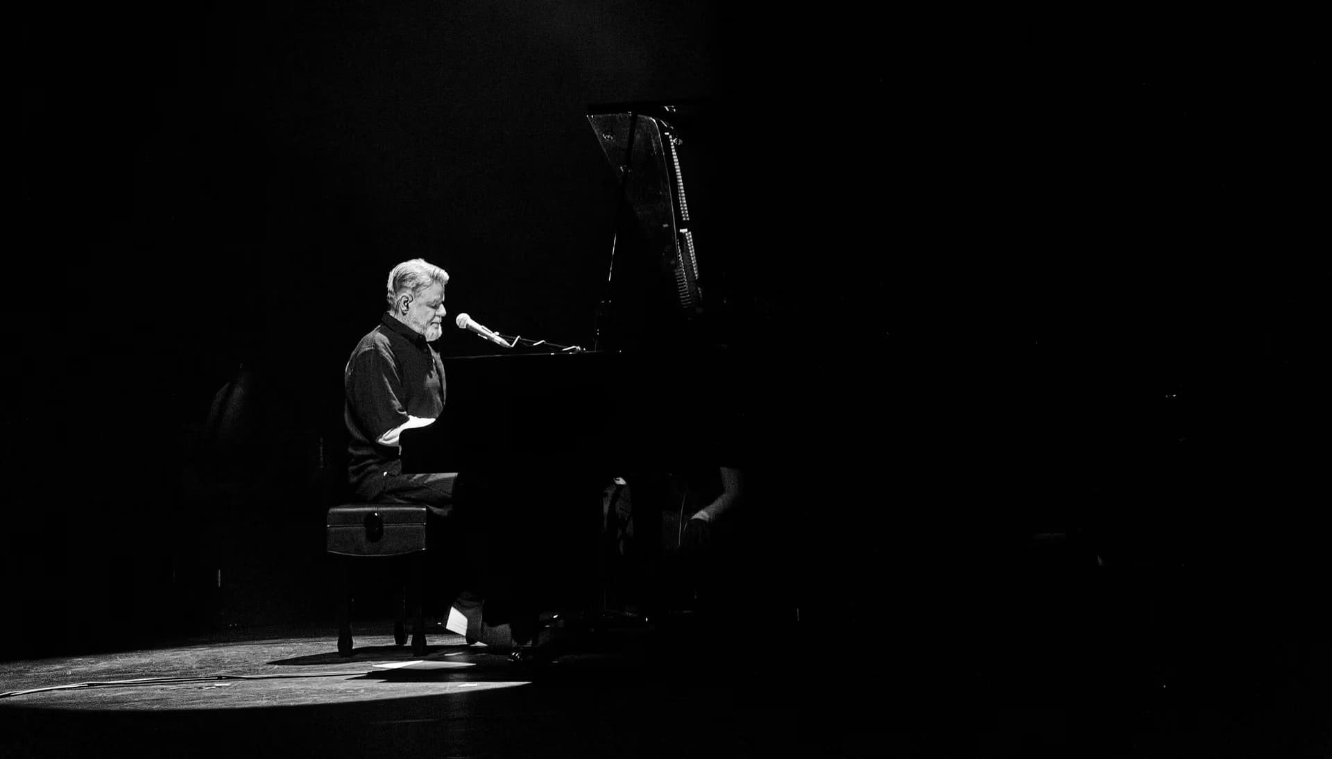 A pianist performs on a dark stage, illuminated by a single spotlight.