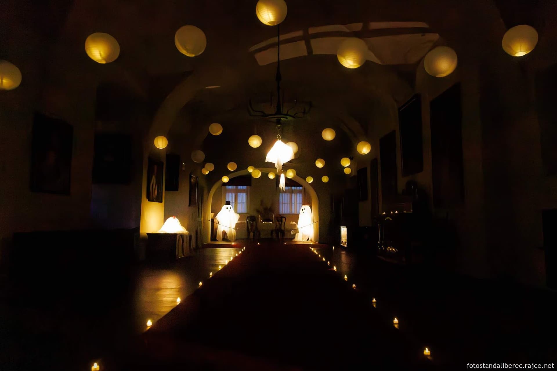 A dimly lit indoor hallway decorated with hanging paper lanterns, small floor candles, and ghost figures.