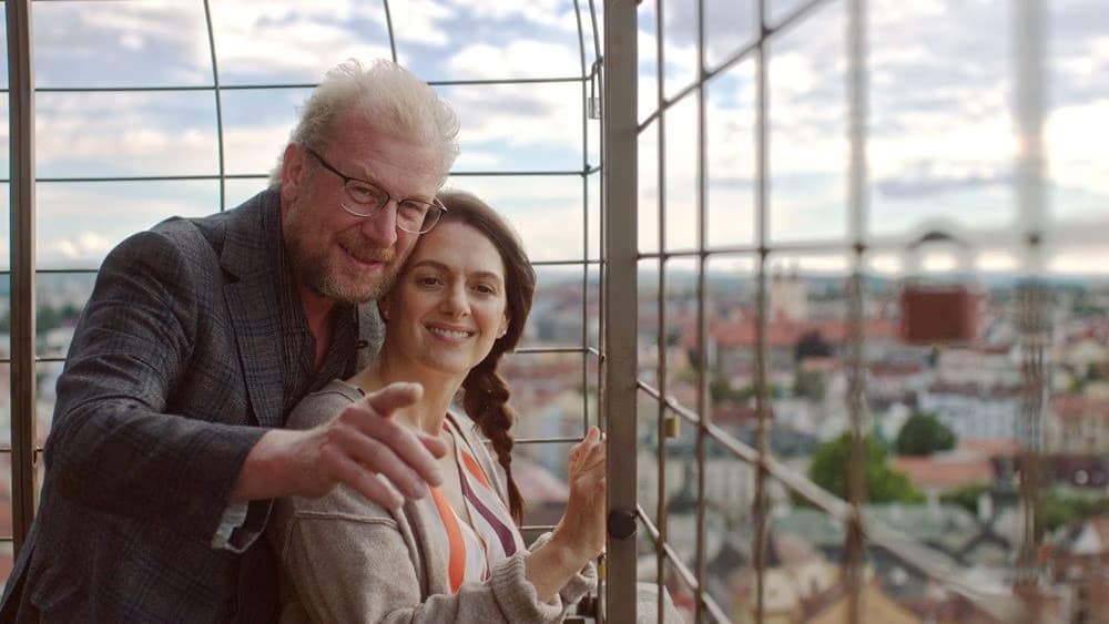 Ein Paar mittleren Alters schaut bei Sonnenuntergang von einer Aussichtsplattform auf die Stadt.
