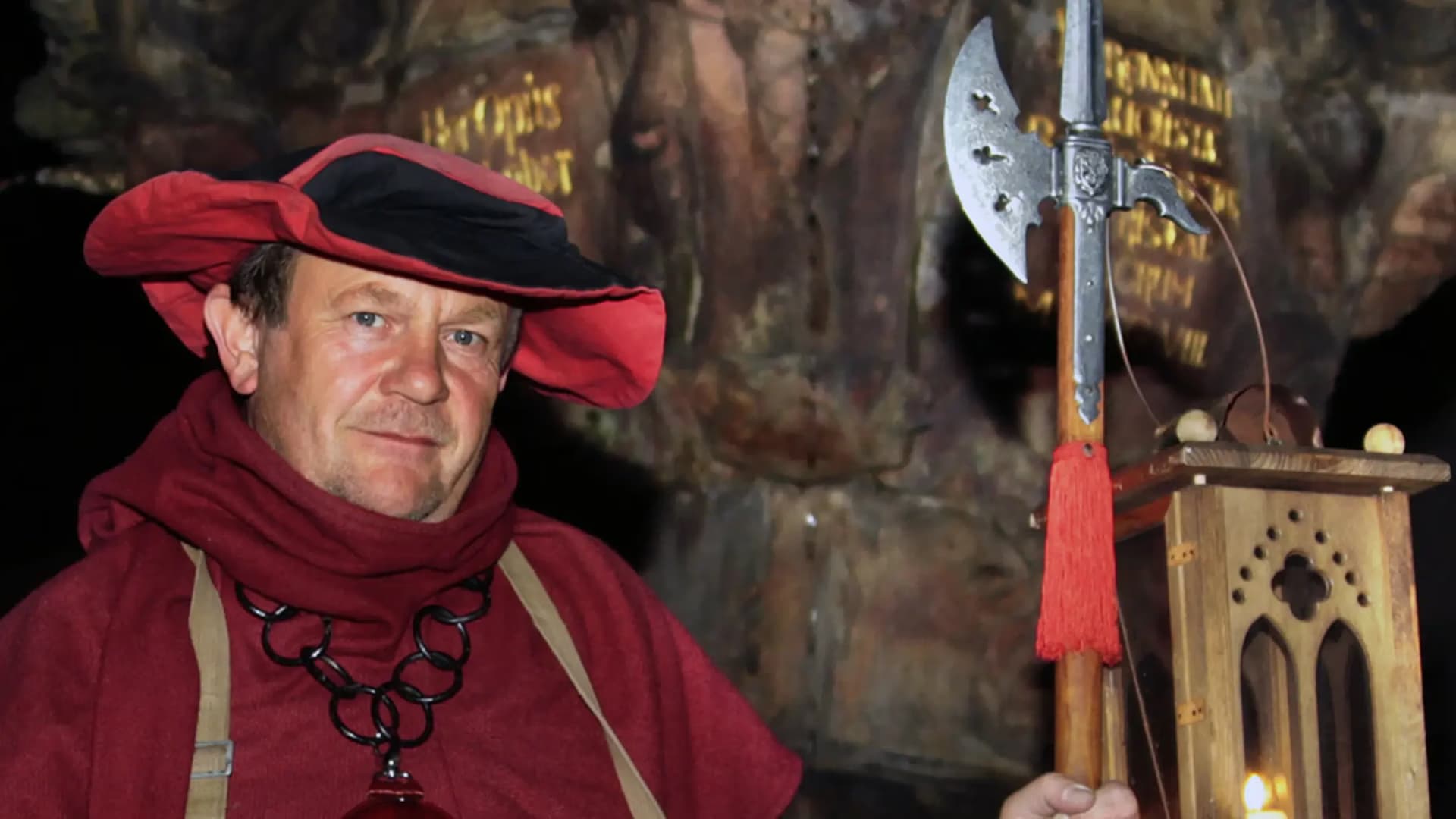 Night watchman in medieval costume holding a halberd and lantern outdoors at night.
