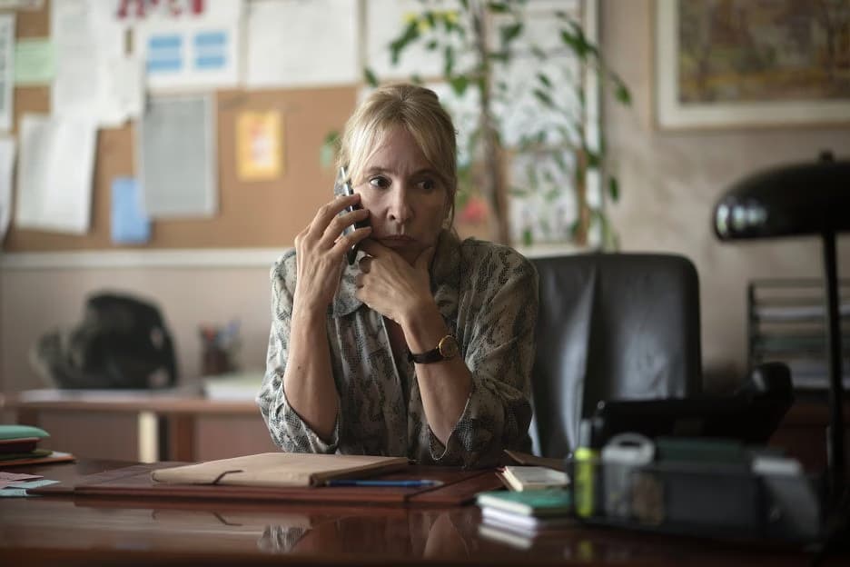 A blonde woman sits at an office desk while talking on a landline phone.