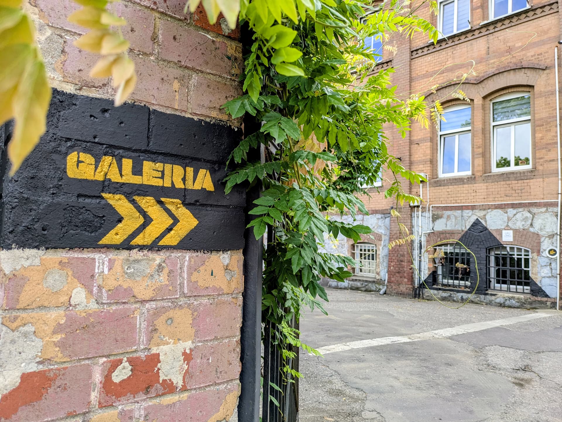Namalovaný černý nápis na cihlové zdi s žlutými šipkami ukazuje cestu do galerie.