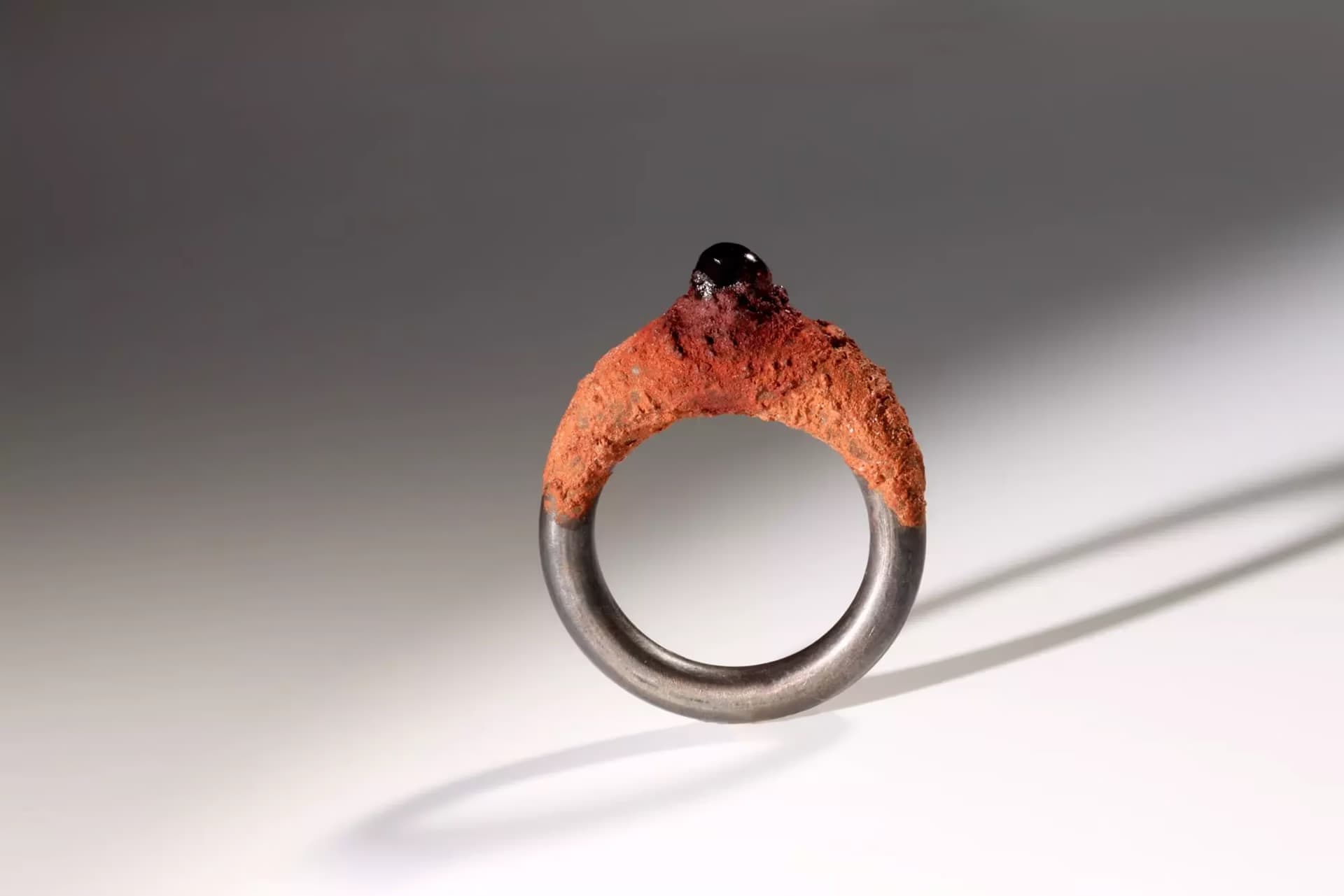 A unique ring features a textured orange top part with a small dark stone against a grey background.