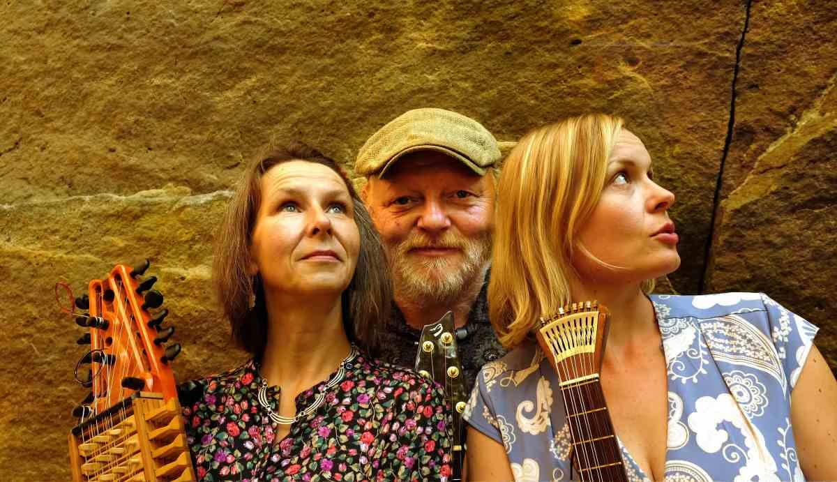 Drei Musiker mit Nyckelharpa und Gitarre posieren vor einer strukturierten Felswand.