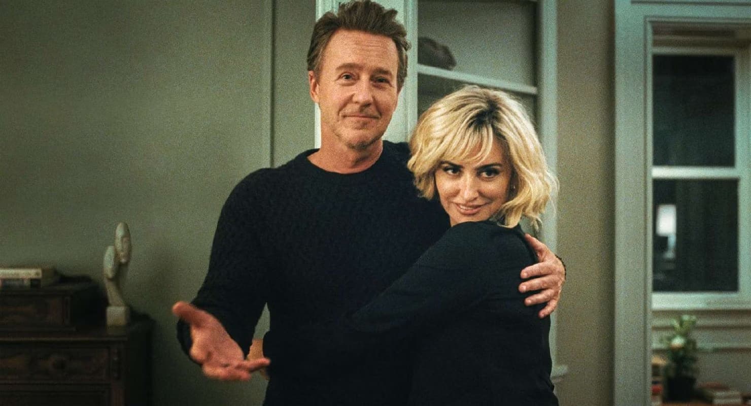 Edward Norton and a blond woman embrace in a brightly lit interior.