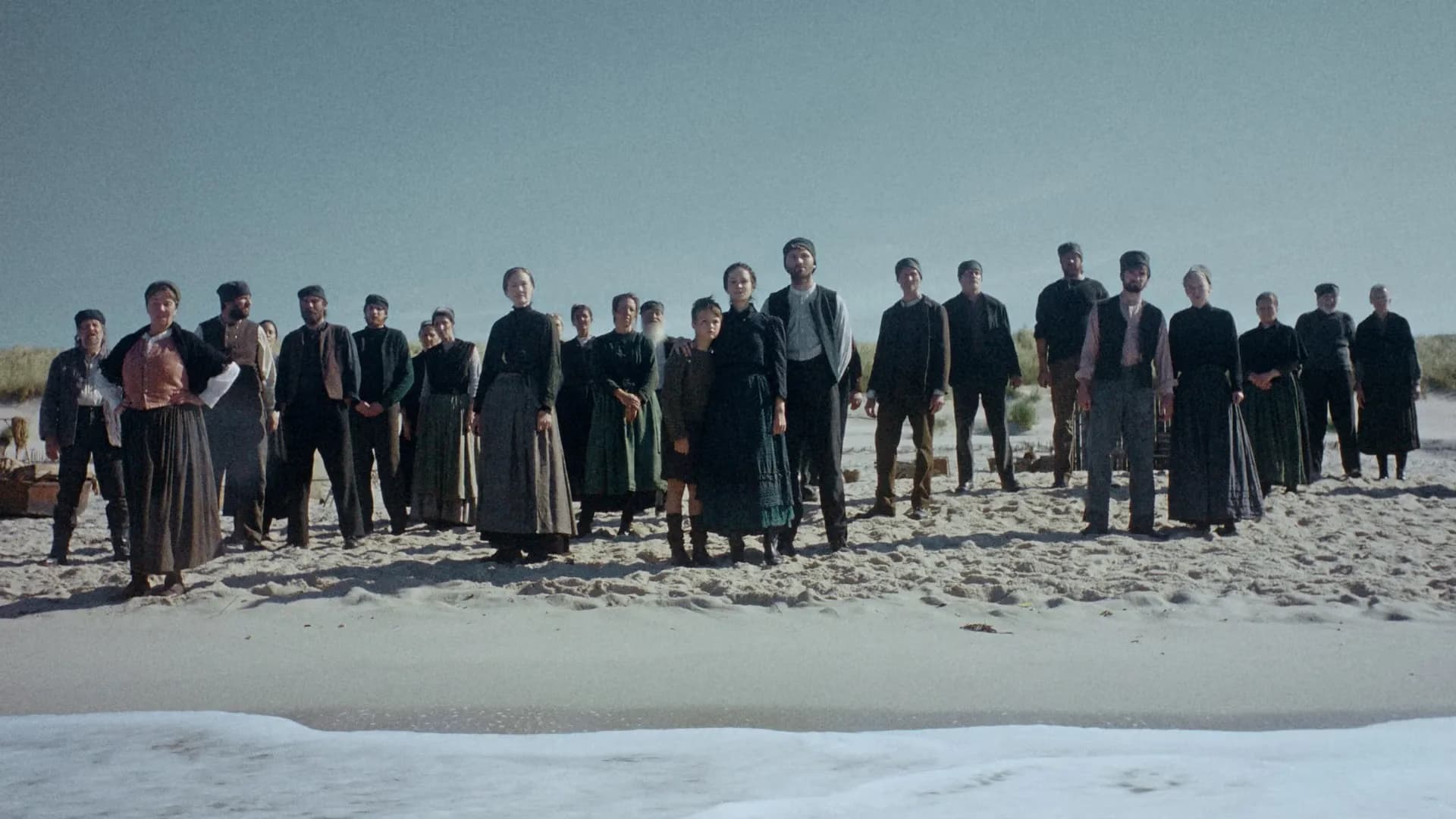 Grupa ludzi w strojach historycznych stoi razem na piaszczystej plaży.