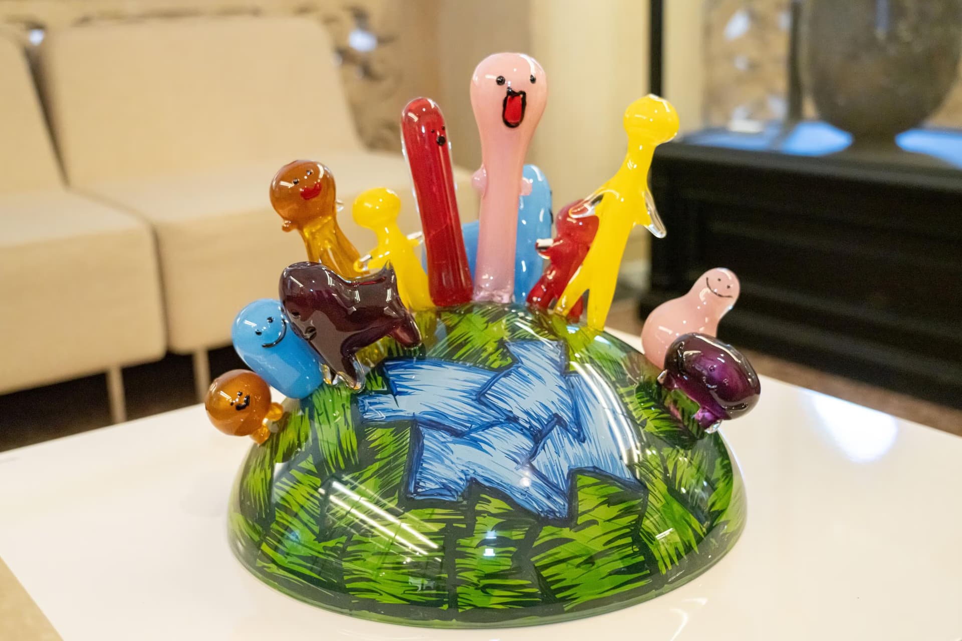Colorful glass sculpture featuring cartoonish creature figures on a dome base.