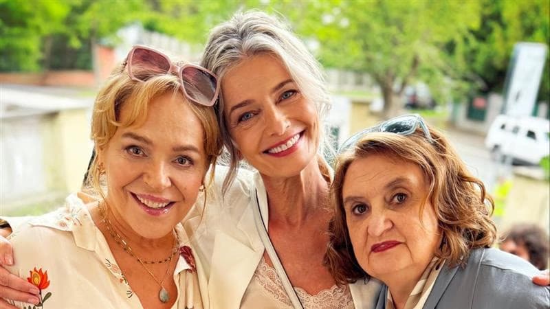 Three smiling women posing together outdoors during a sunny day.