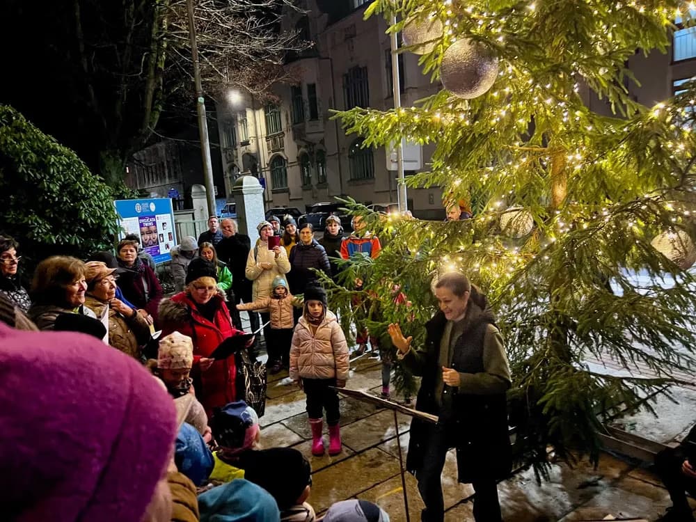 People gather at night around an illuminated Christmas tree during an outdoor holiday event.