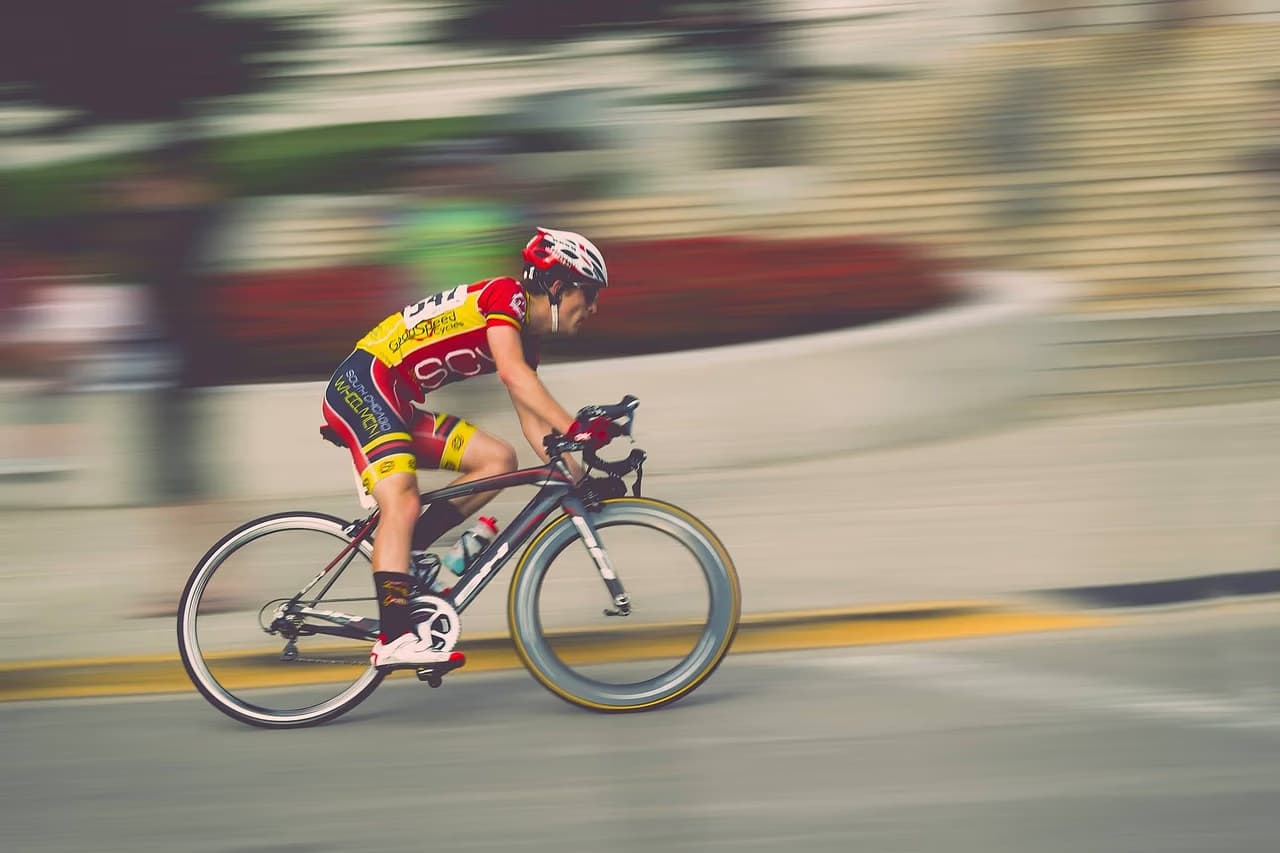 A cyclist in red and yellow jersey speeds along a paved road with motion blur.