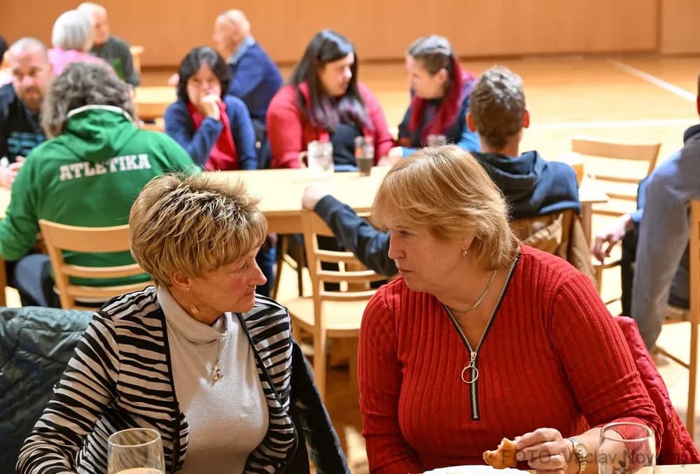 Gruppe von Menschen an Tischen in einer Halle, eine Frau im Vordergrund isst.