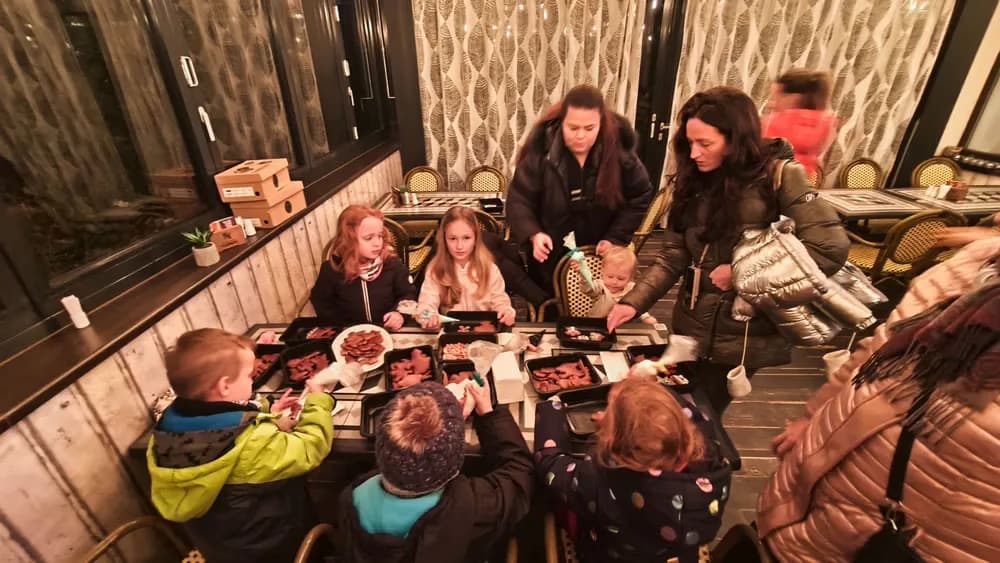 Kinder und Erwachsene sitzen an einem langen Tisch und essen Takeaway-Essen in einem Restaurant.