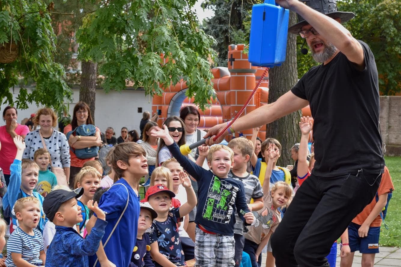 A man in a black shirt performing magic or entertainment for a crowd of children outdoors.