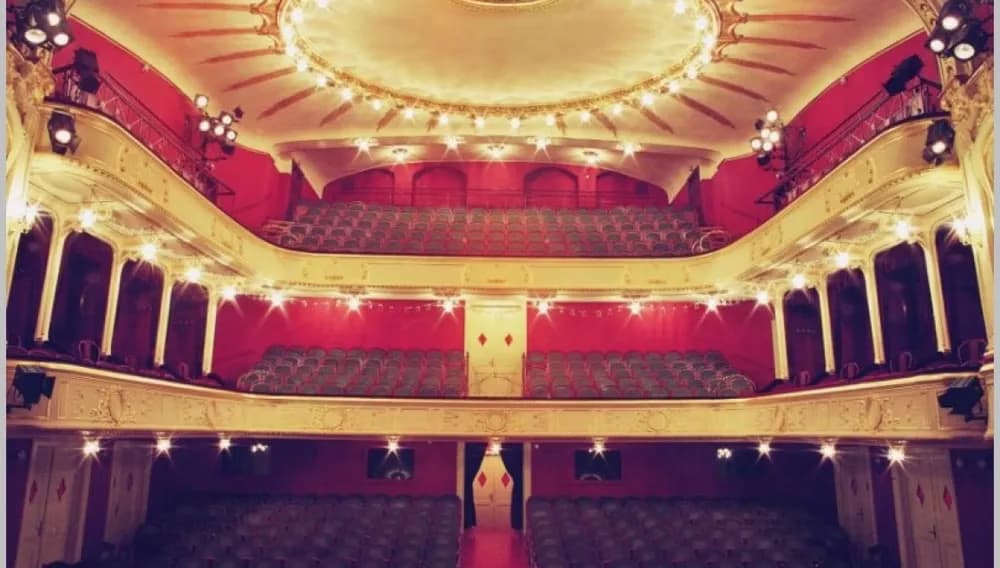 Eleganter mehrstöckiger Theatersaal mit roten Sitzen und goldenen Balkonen unter warmem Licht.