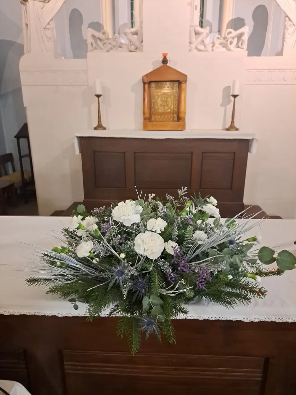 Slavnostní květinová vazba s bílými karafiáty a jehličím stojí na oltáři v kostele.