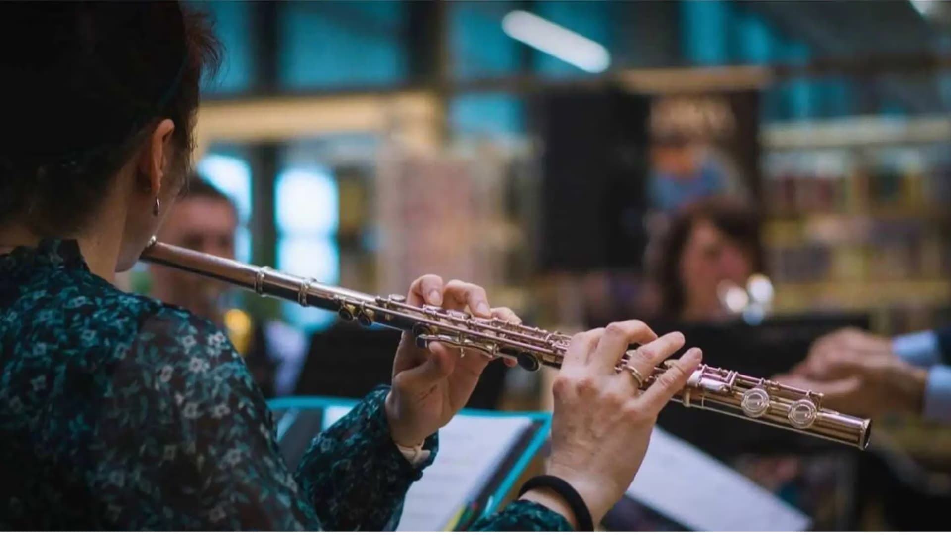 A woman playing a silver transverse flute in an indoor ensemble setting.