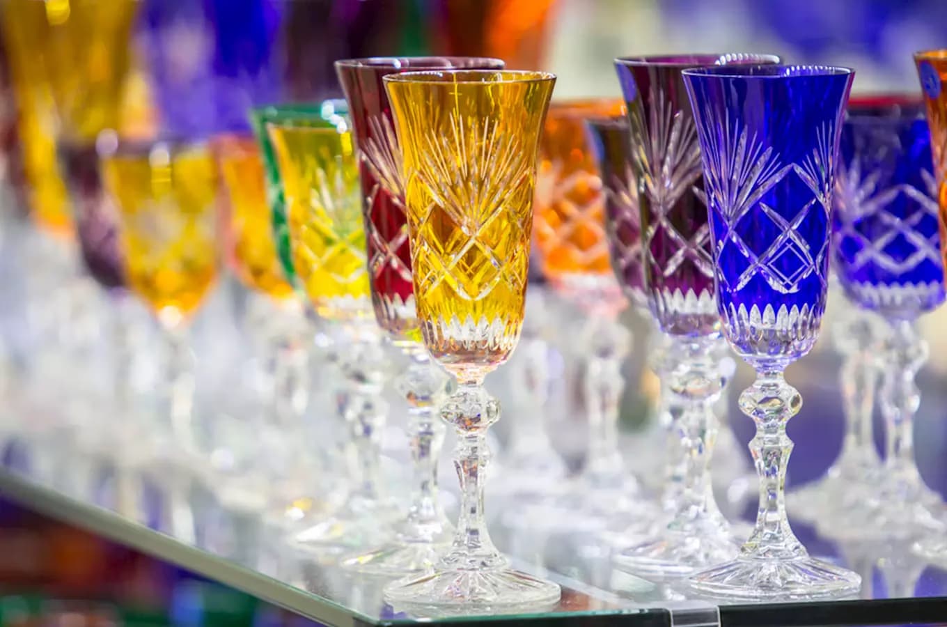 A row of colorful, intricately cut glass goblets displayed on a shelf.