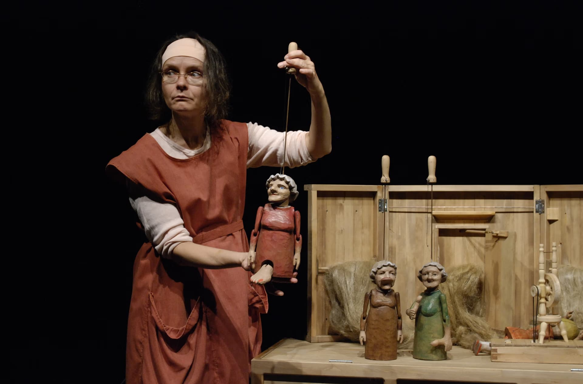 A woman in a rustic costume operates a puppet on stage with other small figures nearby.