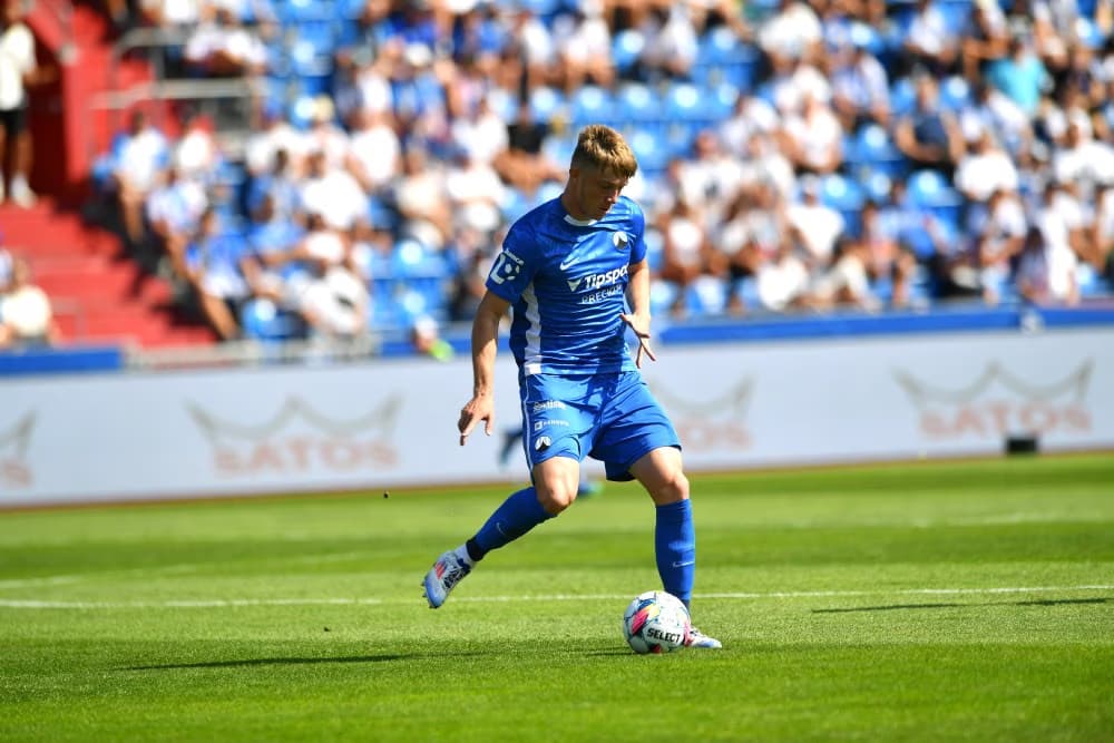 A soccer player in a blue uniform dribbles a ball on the grass during a stadium match.