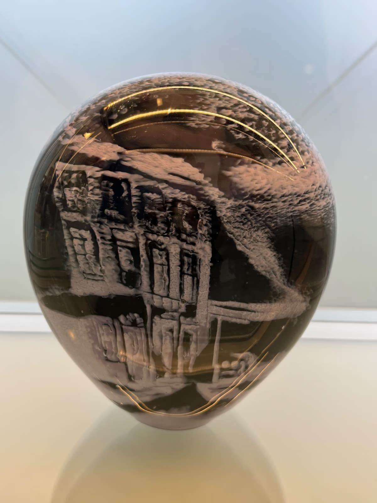 A glass, egg-shaped sculpture with an etched engraving of a building on its surface.