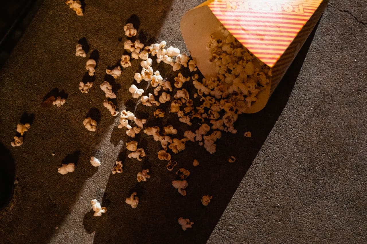 Popcorn spills from a striped cardboard bucket onto dark concrete floor.