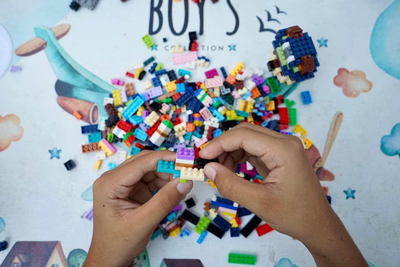 Person's hands assembling colorful plastic building bricks on a patterned play mat.