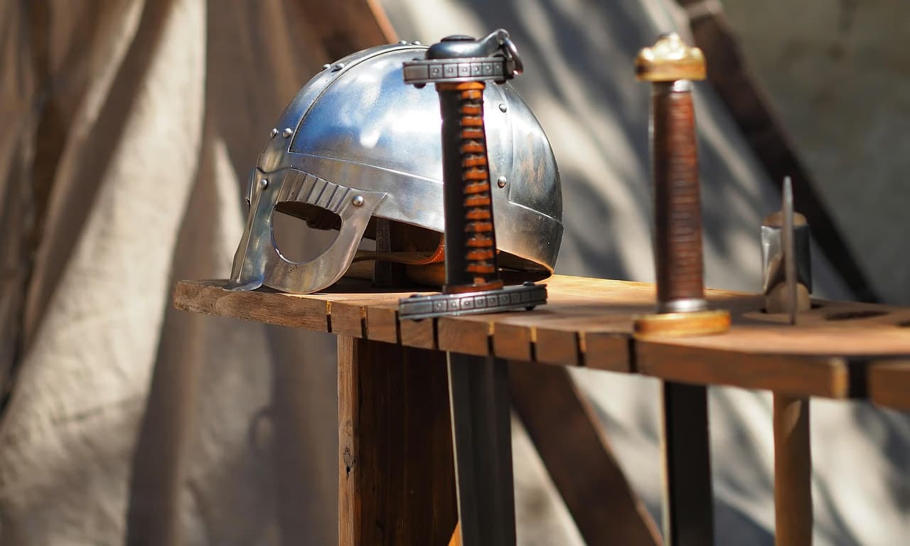 A shiny Viking-style helmet and two swords rest on a wooden display stand.