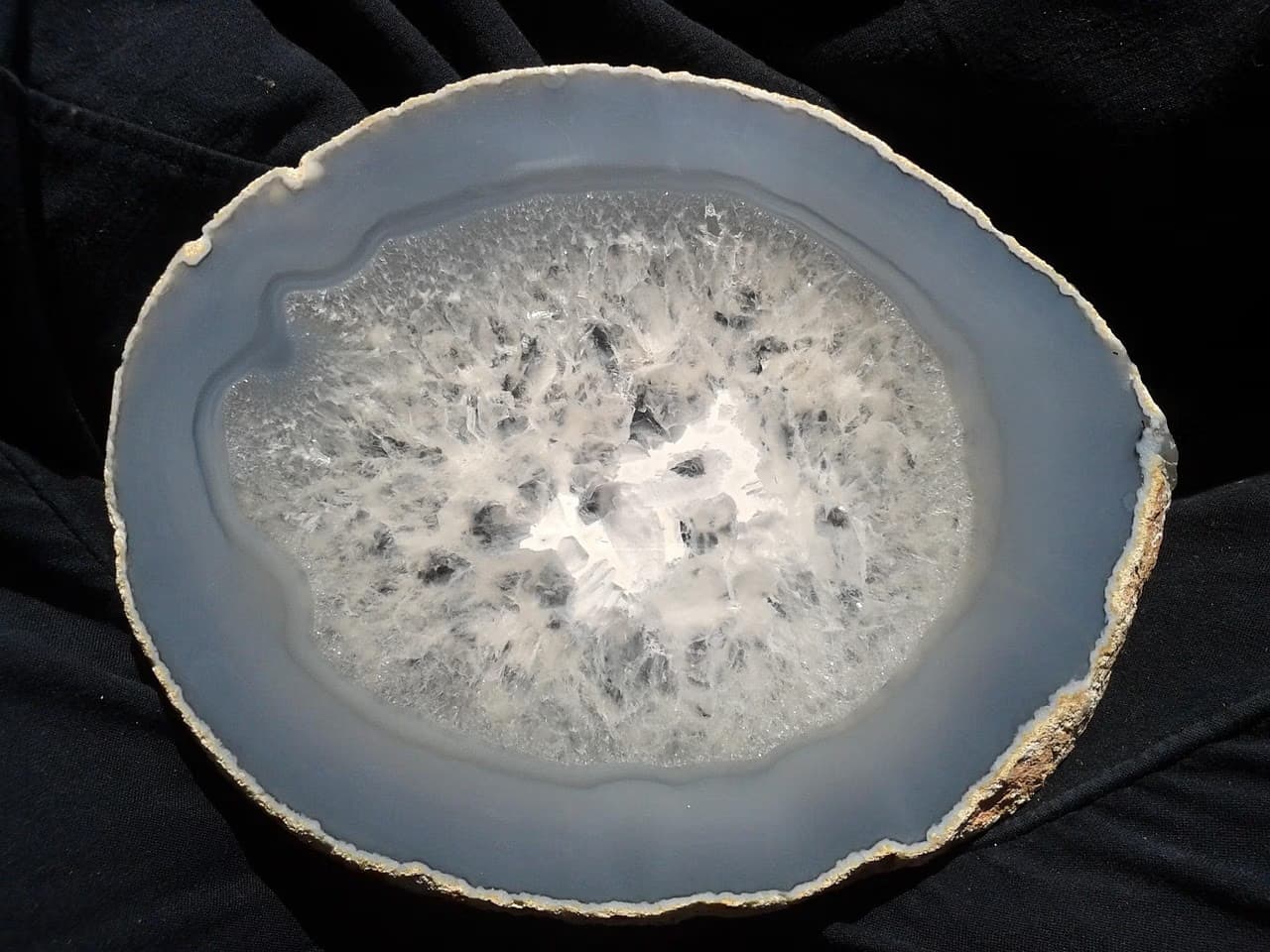 A circular slice of gray and white crystalline agate resting on a dark surface.