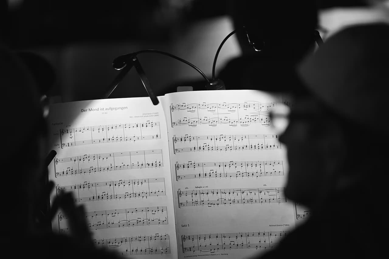 Sheet music stands illuminated by a clip light in a dimly lit, out of focus concert setting.