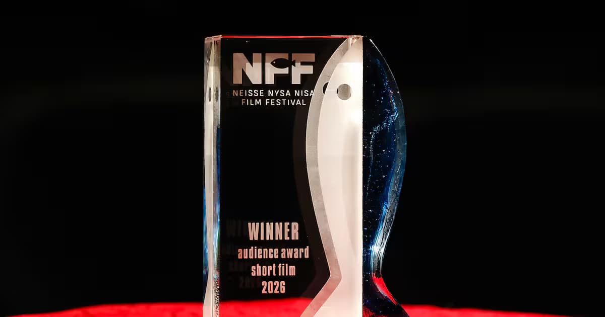 A glass film festival award trophy stands on a red surface against a black background.
